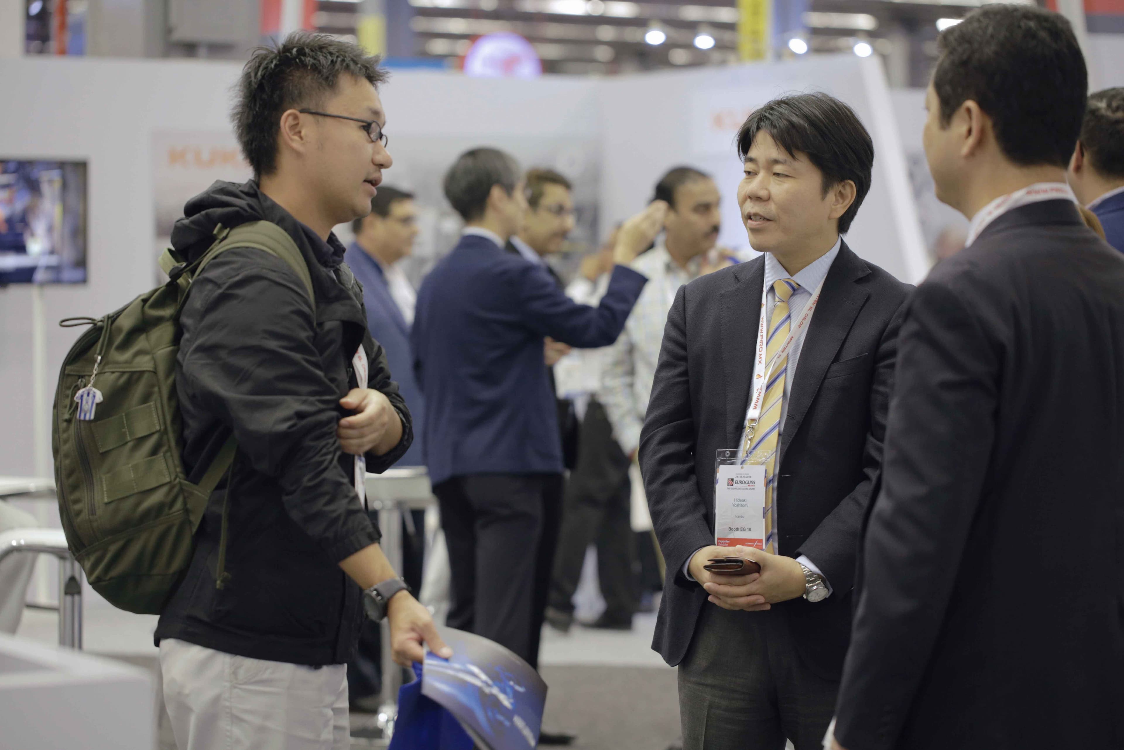 Man with a bagpack talks to two guys in suits