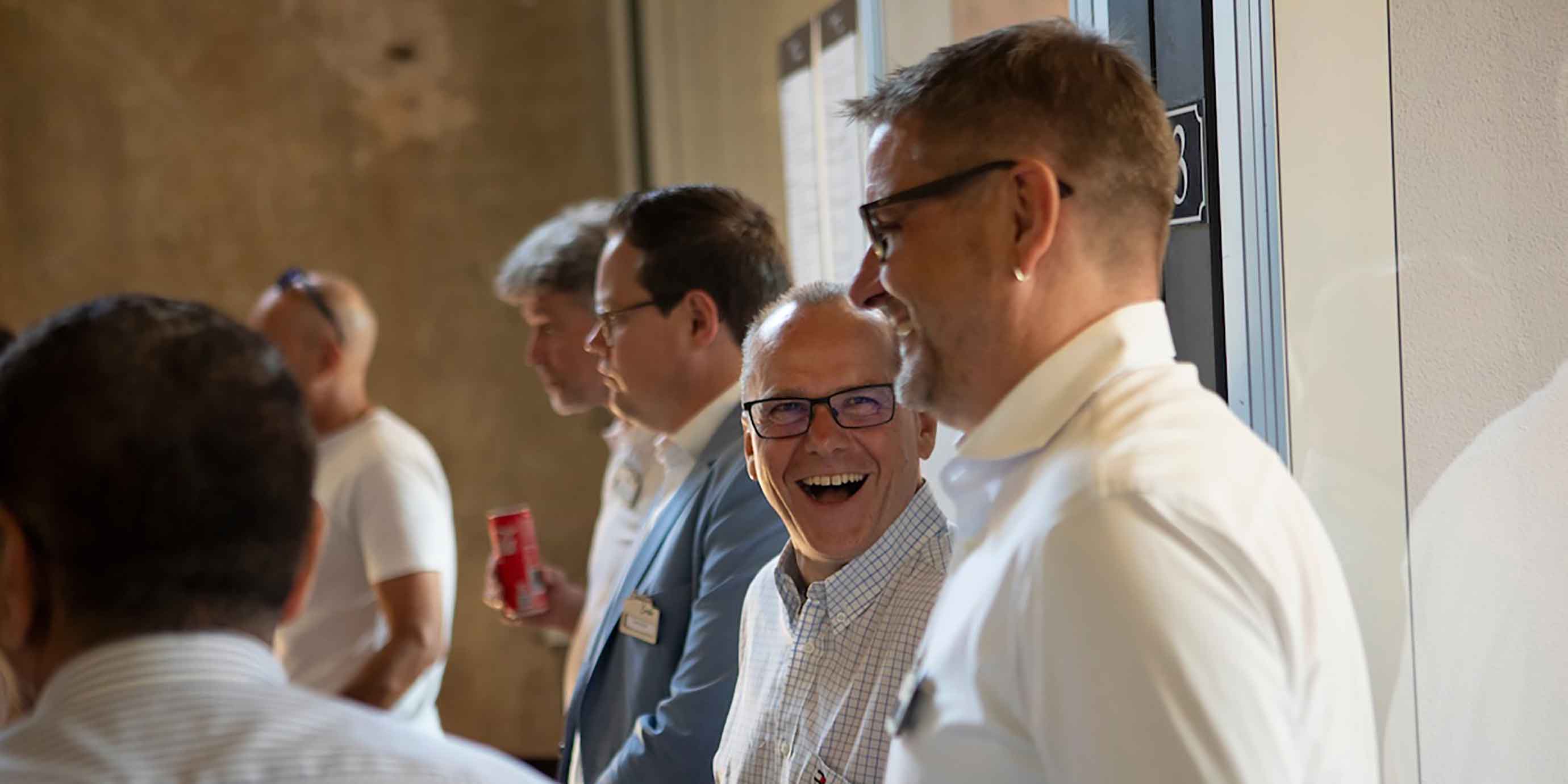Personen im Gespräch in einem Konferenzraum – Business Casual, Namensschilder, Holzbalkendecke im Hintergrund.